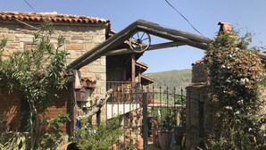 Una casa de piedra rústica con un balcón de madera, una verja metálica y macetas con plantas.