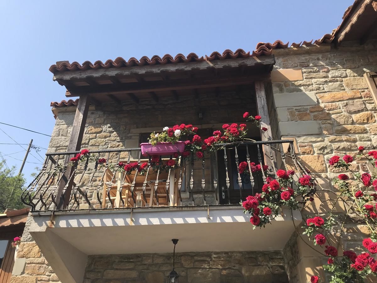 A stone building with a balcony adorned with red flowers and a wooden chair.