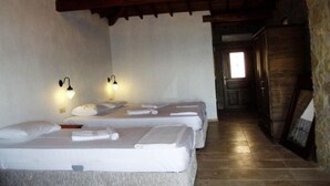 Habitación con tres camas, cada una con ropa y toallas blancas, y dos lámparas de pared.
