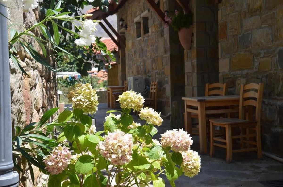 A stone building with a wooden table and chairs, surrounded by greenery and flowers.