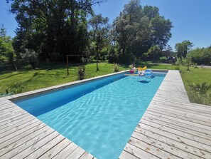 Ein rechteckiger Pool mit klarem, blauen Wasser, umgeben von einer Holzterrasse und einer Rasenfläche mit Bäumen.