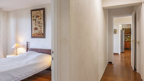 Een slaapkamer met een bed, een nachtkastje, een lamp en een kunstwerk aan de muur.