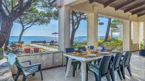 Una zona de menjador a l'aire lliure amb vista al mar, amb una taula coberta de plats, gots i un bol de amanida.