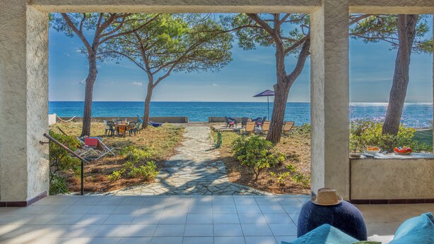 Une vue depuis un espace extérieur abrité, avec un chemin de pierre menant à un coin salon situé au bord de la mer.