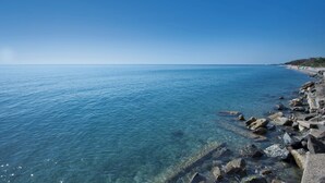Un paysage côtier avec une eau bleue et limpide, une côte rocheuse et une plage lointaine où se trouvent des personnes.