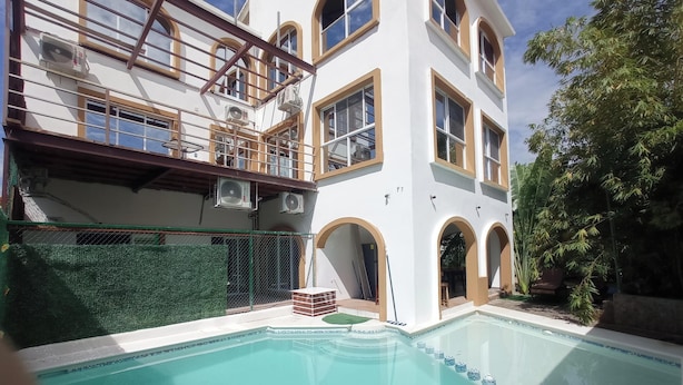 A two-story building with a swimming pool, outdoor seating, and a fenced area with greenery. - PALMAS DE CHAHUE 1 (700 SF) (Bahías de HUATULCO)