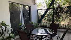 A round table with four chairs in a covered outdoor area with a view of greenery through a wire mesh. - PALMAS DE CHAHUE 1 (700 SF) (Bahías de HUATULCO)