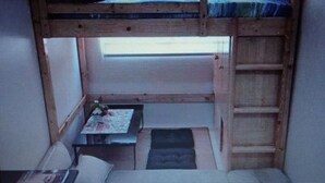 Ein kleiner, schummrig beleuchteter Raum mit einem Etagenbett, einem Schreibtisch und einem Stuhl.