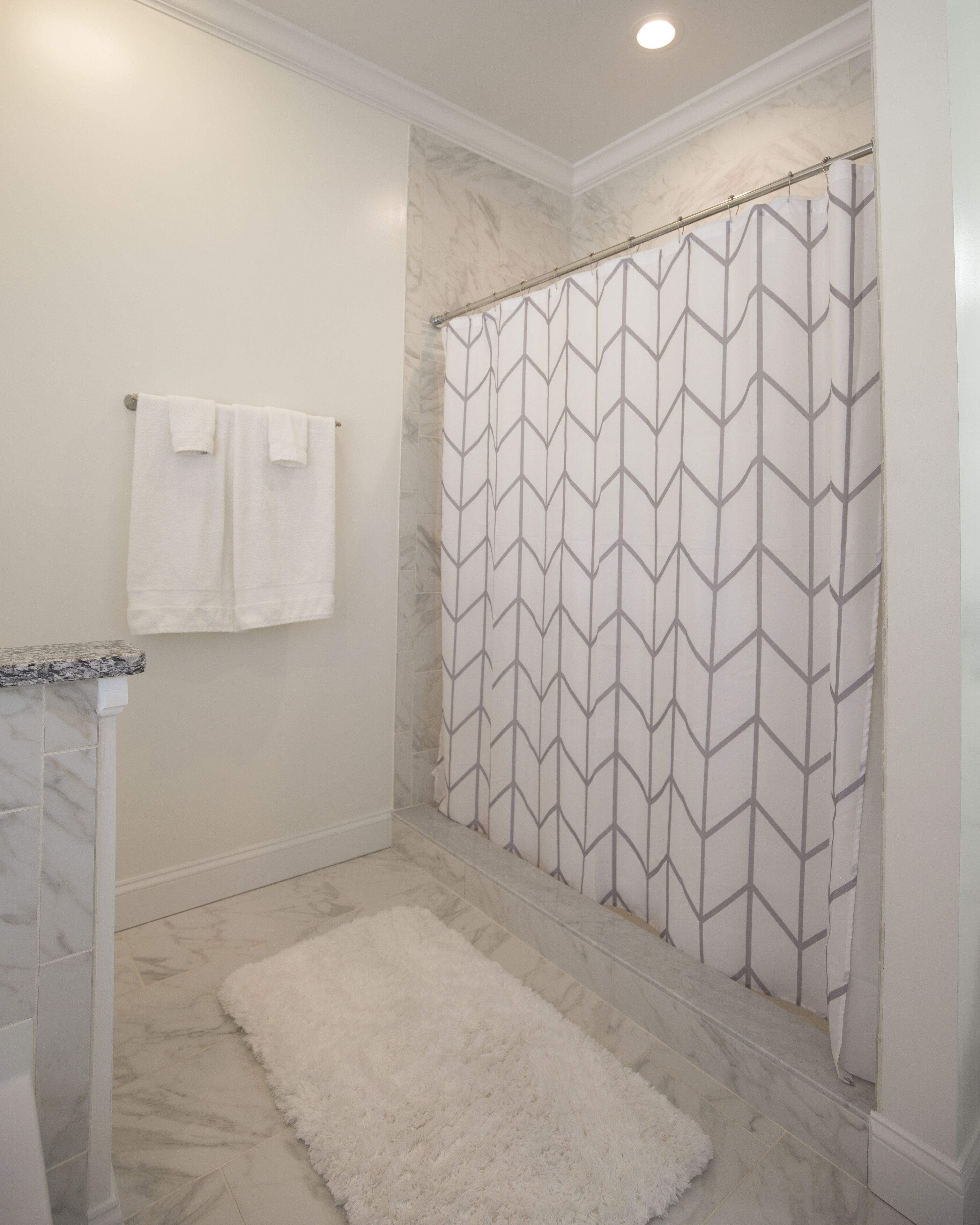 Un baño con cortina de ducha, una alfombra blanca y esponjosa, y una toalla colgada en la pared.