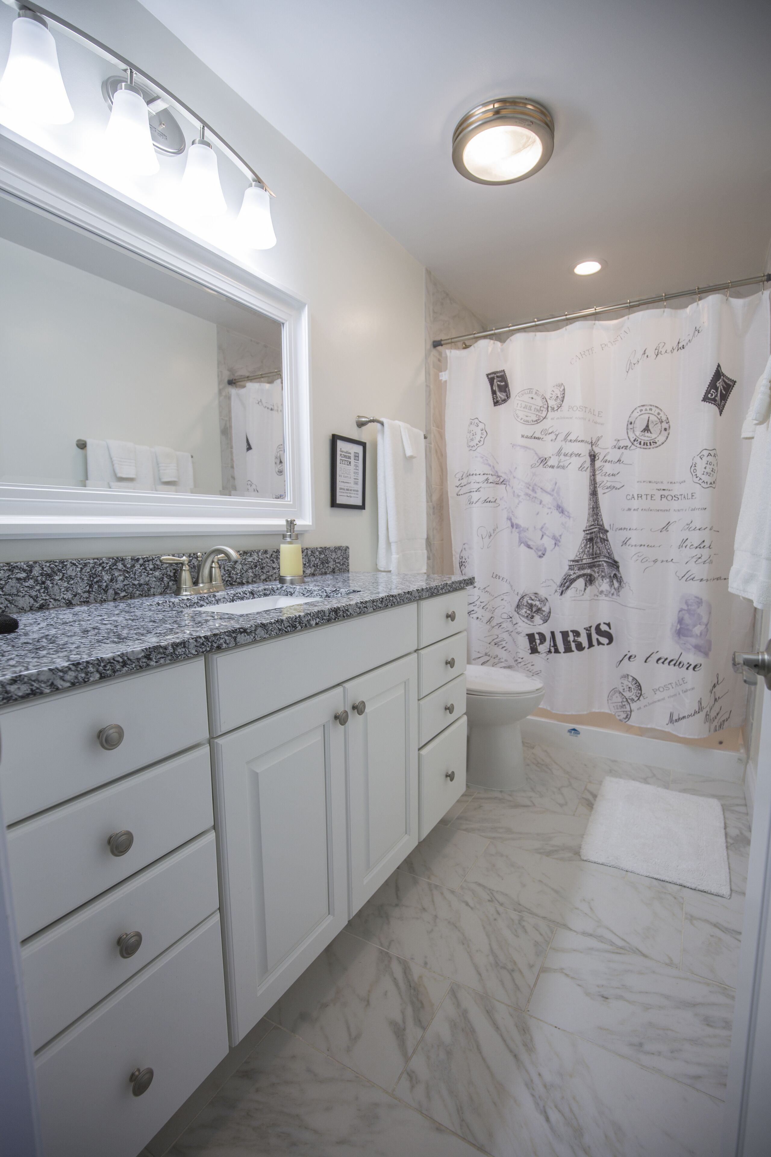 A bathroom with a marble floor, a sink with a mirror, and a shower curtain with Paris-themed designs.