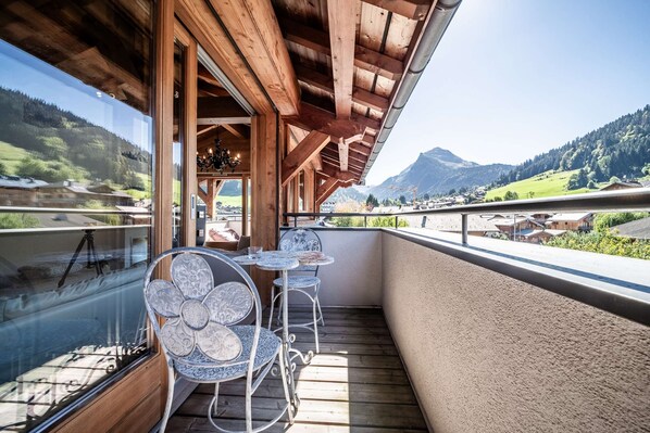 A wooden balcony with a table and chairs, overlooking a mountainous landscape.