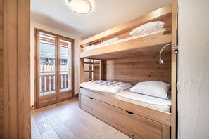 A bunk bed room with a wooden floor, a ceiling light, and a sliding glass door leading to an outdoor area.