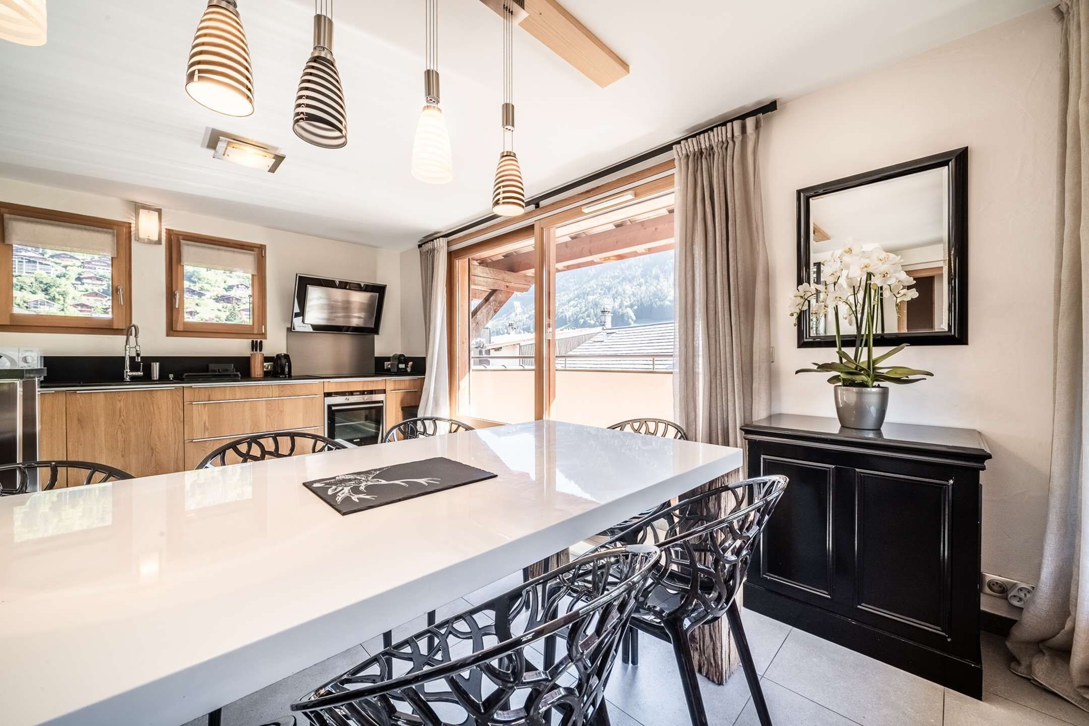 Een moderne keuken met een groot eiland, houten kastjes en een eethoek met metalen stoelen.