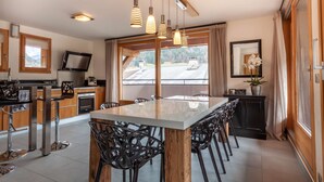 A modern kitchen with a central island, bar stools, pendant lighting, and a large window offering a view of the outdoors.