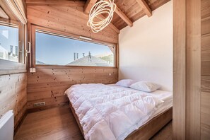 Quarto com uma grande janela, paredes de madeira, cama com roupa de cama branca e luminária no teto.