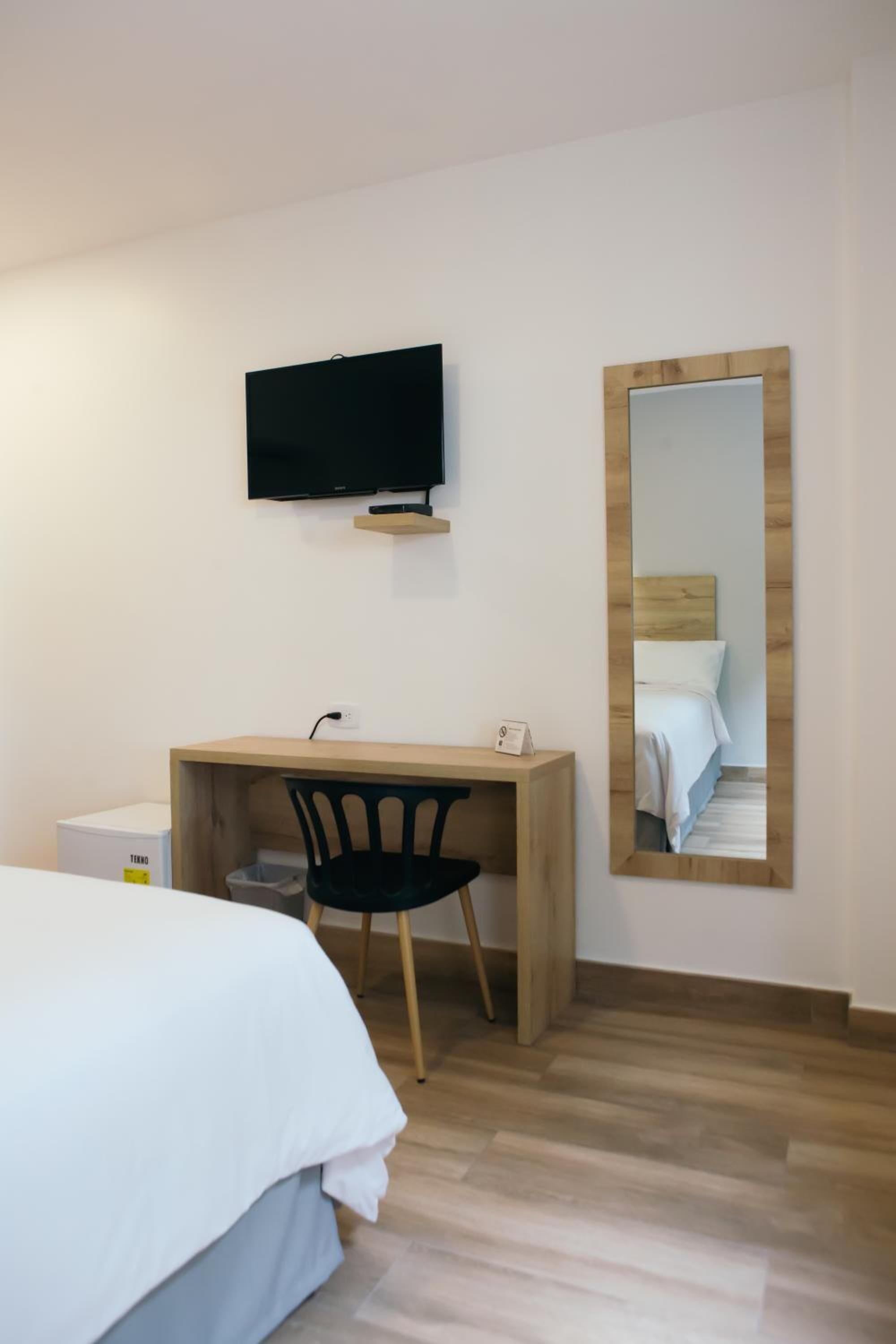 Una habitación de hotel con una cama, un escritorio, una silla, un televisor y un espejo.