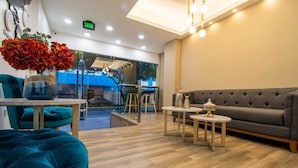 A modern interior with a sofa, teal ottoman, and a table with a vase of flowers. - The Park Hotel (Guayaquil)