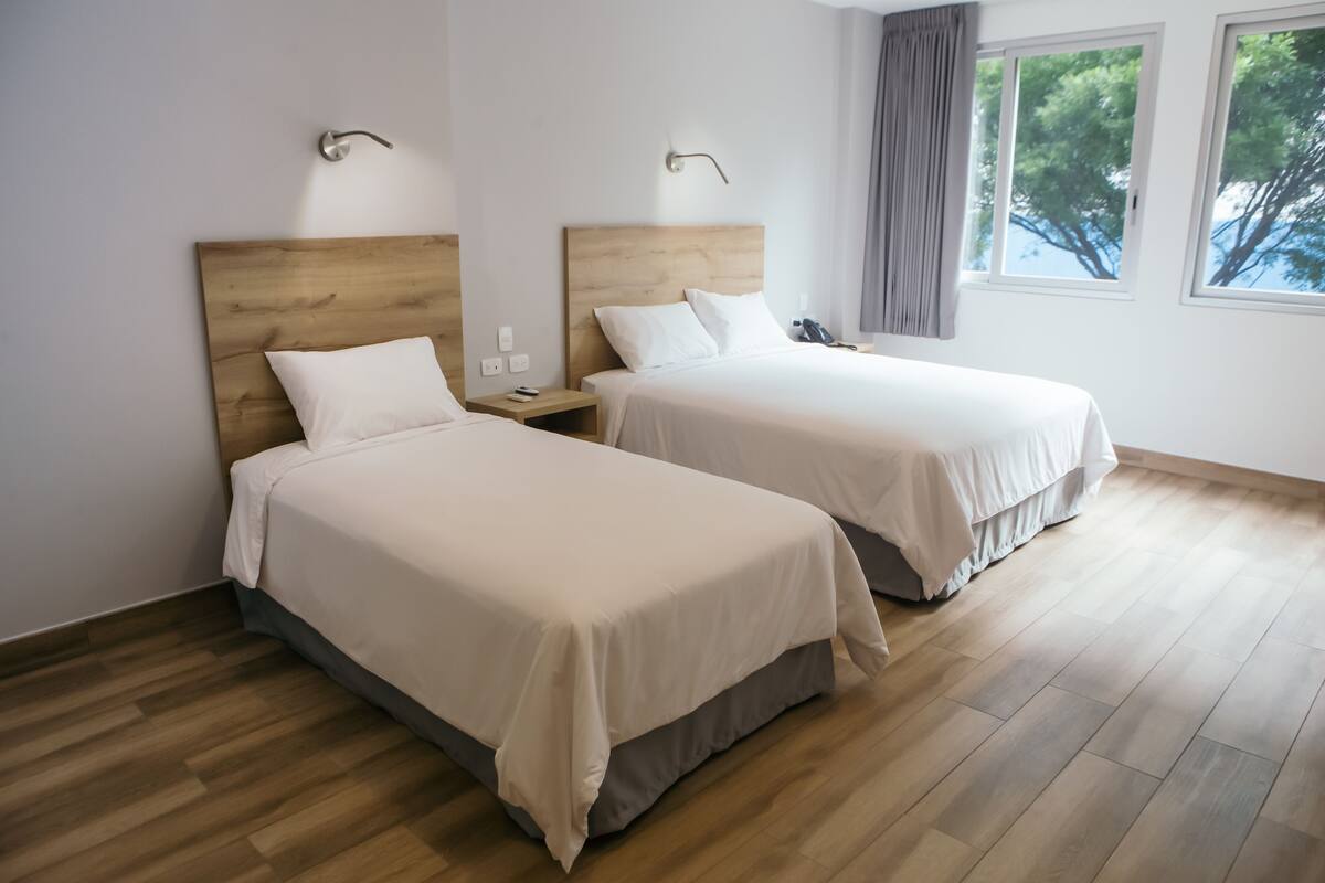 Ein Hotelzimmer mit zwei Betten, Holzboden und einem Fenster mit Blick auf Bäume.