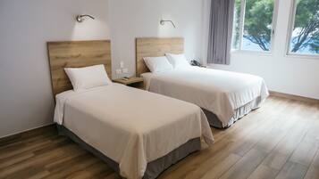 A hotel room with two beds, wooden flooring, and a window with a view of trees.