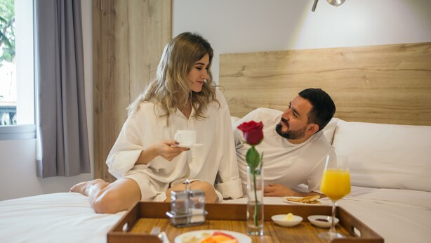A couple in bed with a tray of breakfast including toast, fruit, and juice. - The Park Hotel (Guayaquil)