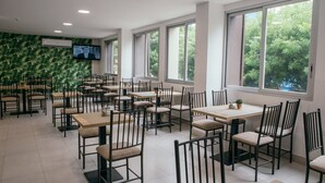 A spacious restaurant with multiple tables and chairs, large windows with a view of trees, and a mounted television on the wall. - The Park Hotel (Guayaquil)