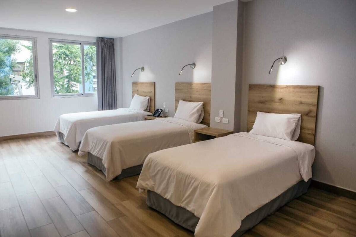 Ein Hotelzimmer mit zwei Einzelbetten, einem Holzkopfteil, einem Nachttisch mit Lampe und einem Fenster mit Vorhängen.