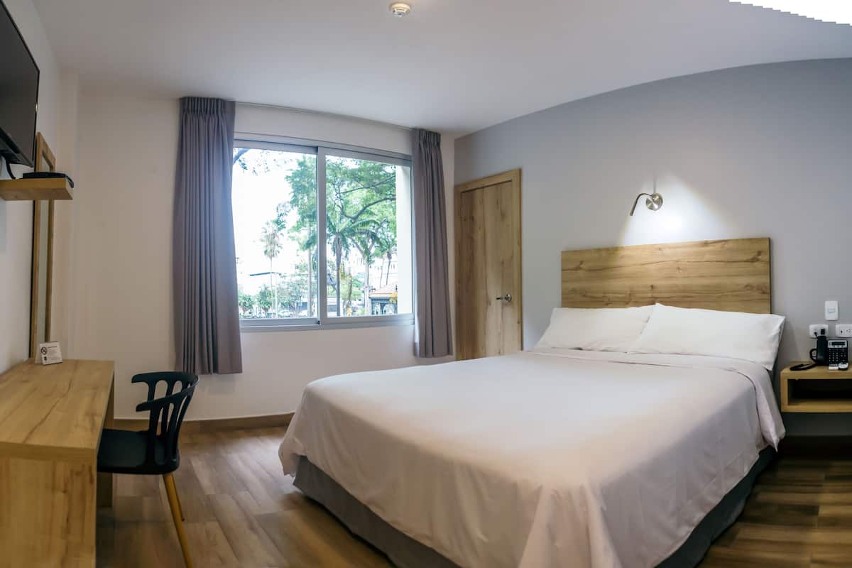 Ein Schlafzimmer mit einem großen Bett, einem Holztisch, einem Stuhl, einem Nachttisch und einem Fenster mit Vorhängen.