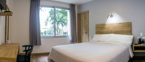 Un dormitorio con una cama grande, un escritorio de madera, una silla, una mesita de noche y una ventana con cortinas.