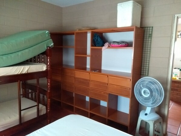 A room with a bunk bed, a wooden dresser with multiple drawers, a small white fan, and a tiled wall.