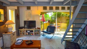 A living room with a television, a sofa, and a coffee table. There is a staircase leading to an outdoor area with a view of greenery.