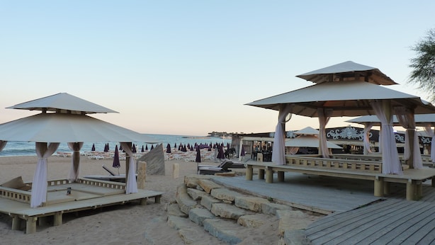 A beach with wooden gazebos, lounge chairs, and umbrellas.