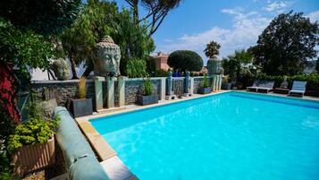 A swimming pool with a stone wall and decorative statues, surrounded by lush greenery and trees.