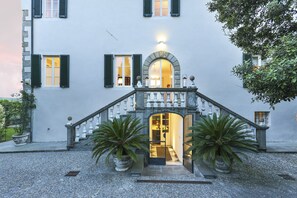 A building with a stone staircase leading to an arched doorway, surrounded by potted plants.