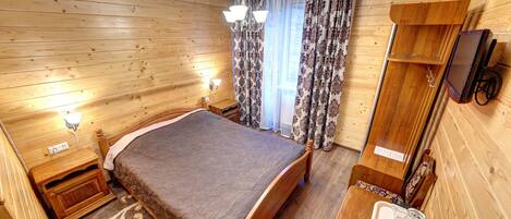 A wooden-paneled room with a bed, bedside table, lamp, and a TV mounted on the wall.