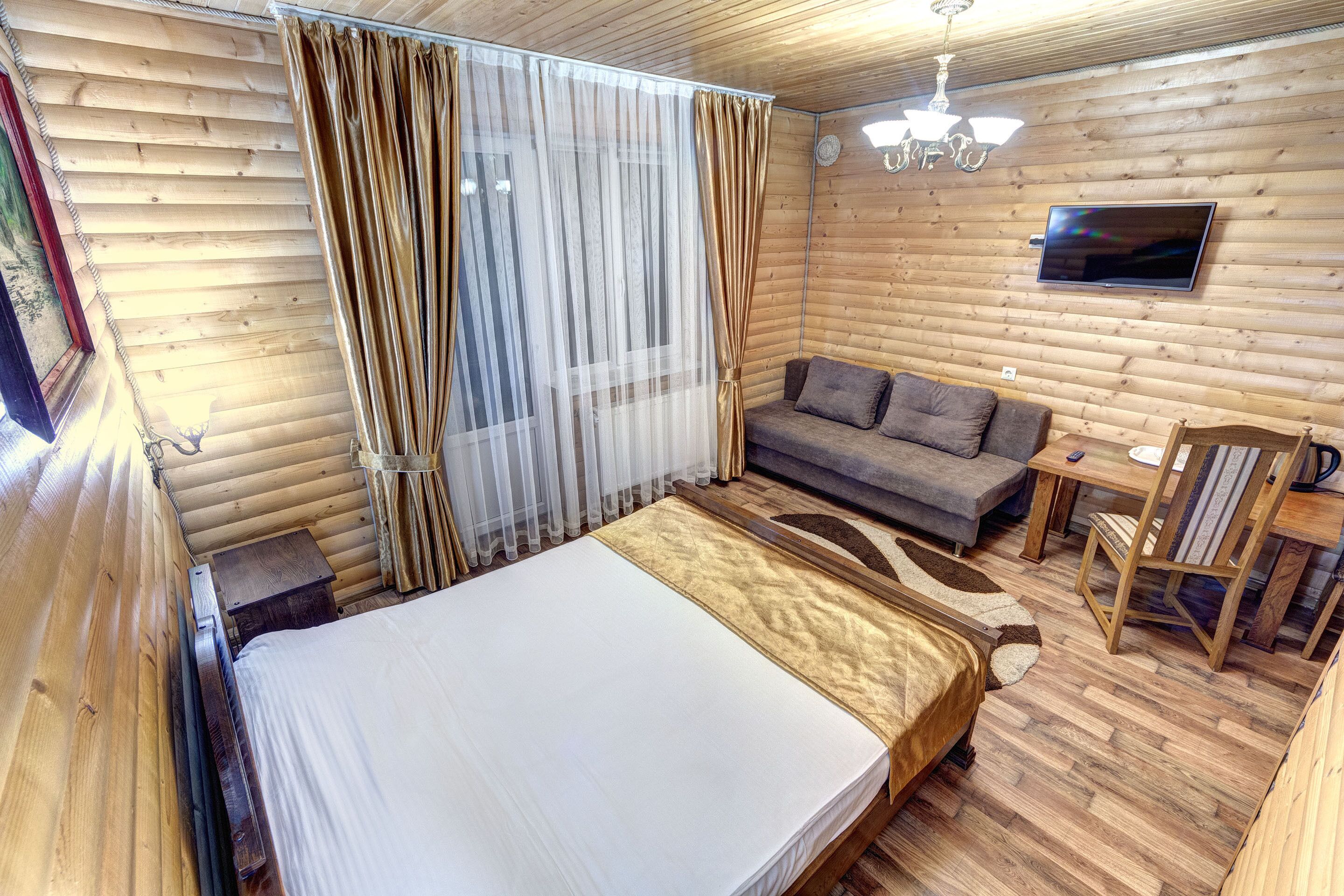 Una habitación de cabaña de madera con una cama, un sofá, un televisor y una mesa de comedor.