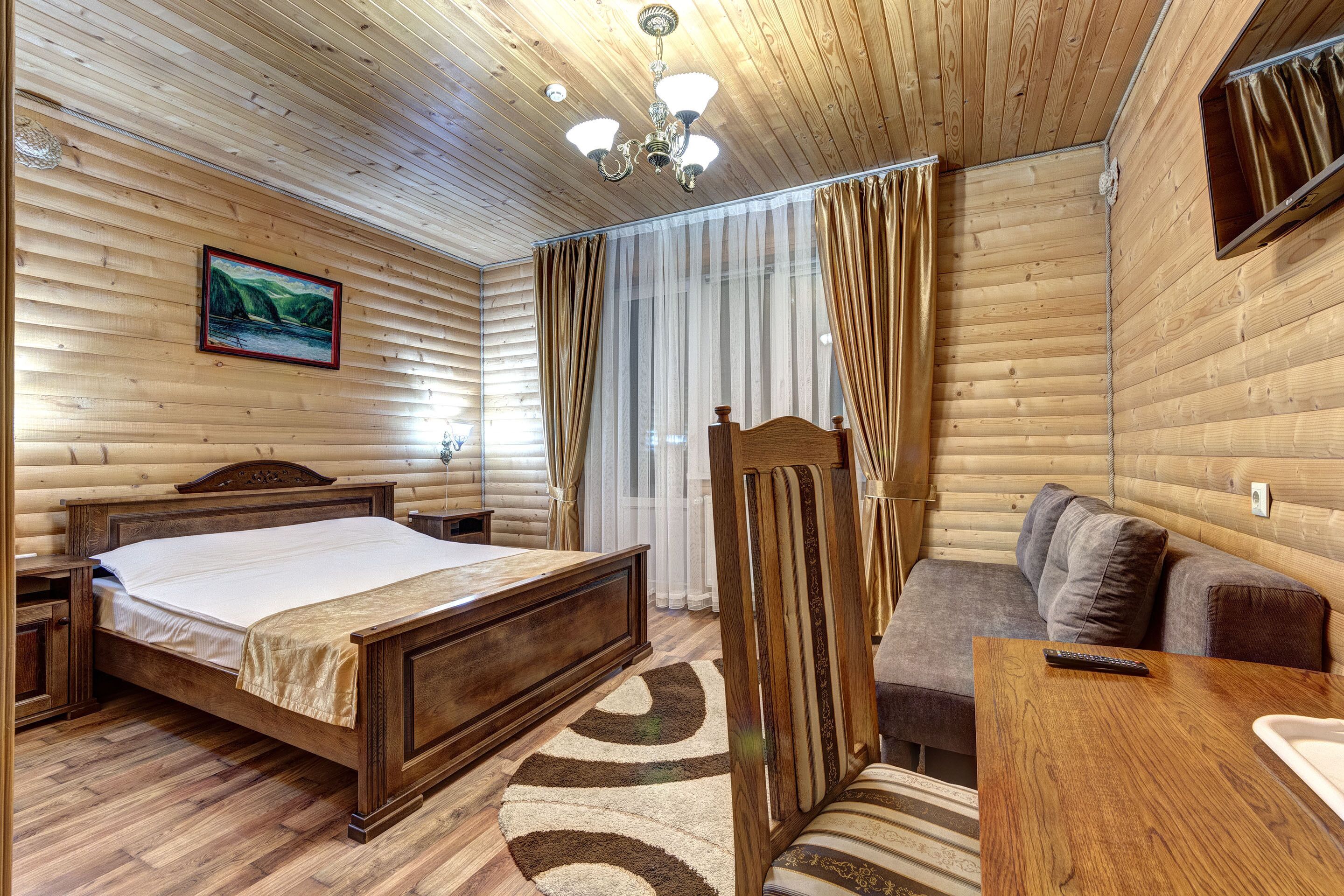 A wooden-paneled room with a bed, a sofa, a small table, and a mirror.