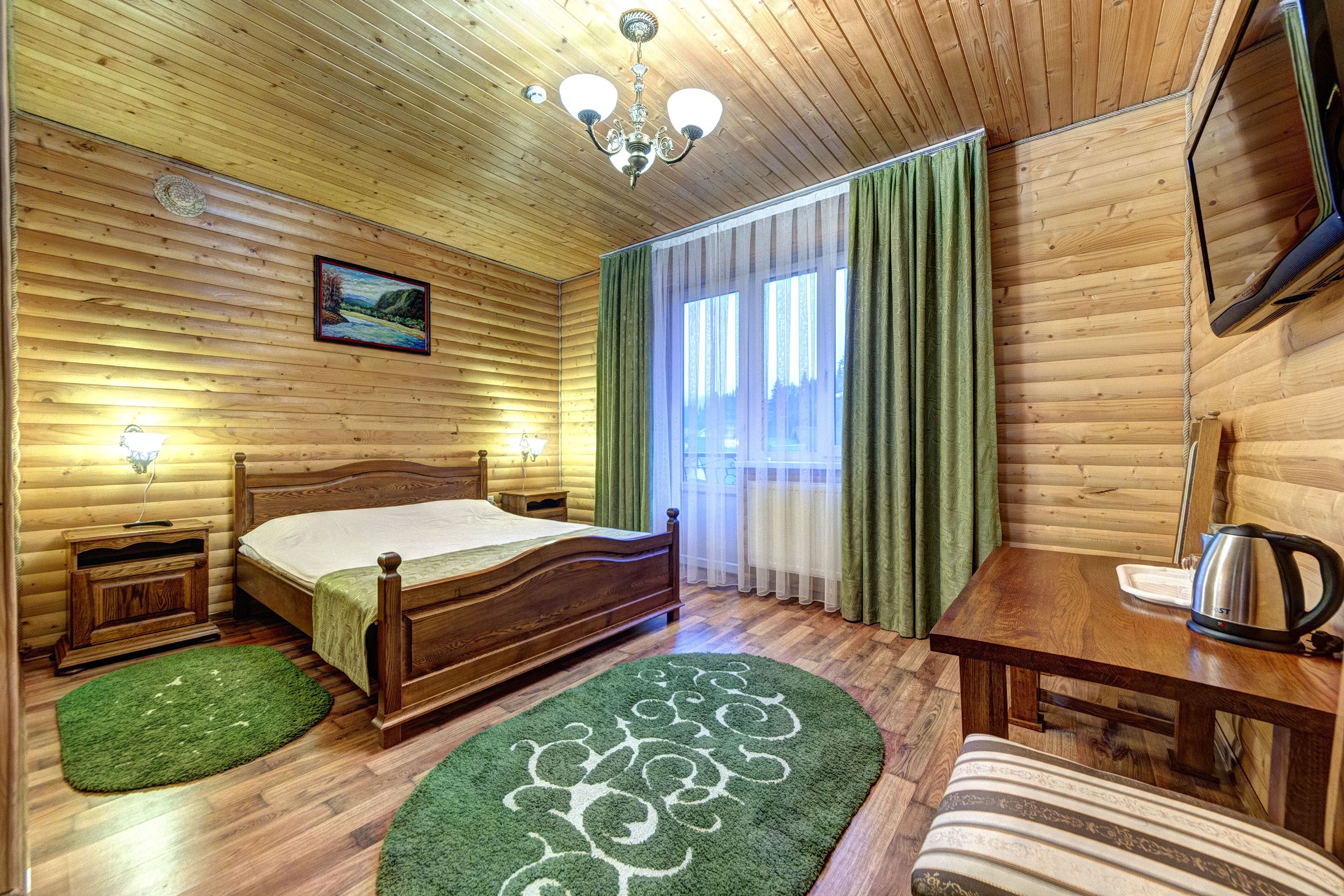 Habitación de cabaña de madera con una cama, un escritorio, una silla, un televisor y una ventana con cortinas.