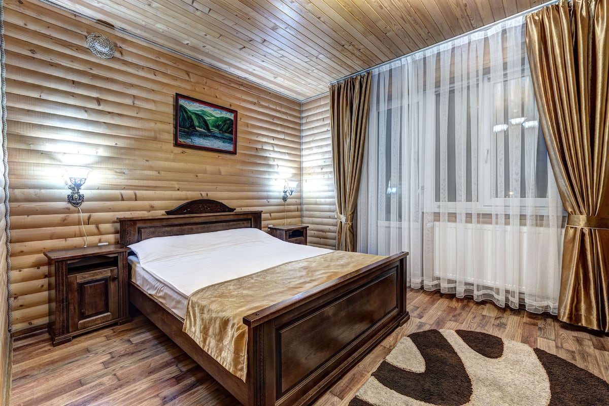 A wooden-paneled room with a bed, nightstands, and a window with curtains.