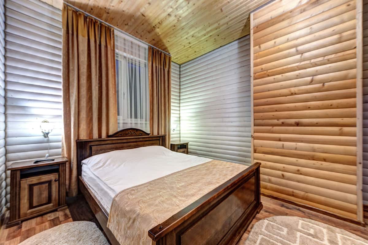 A wooden-paneled bedroom with a bed, nightstands, and a window with curtains.