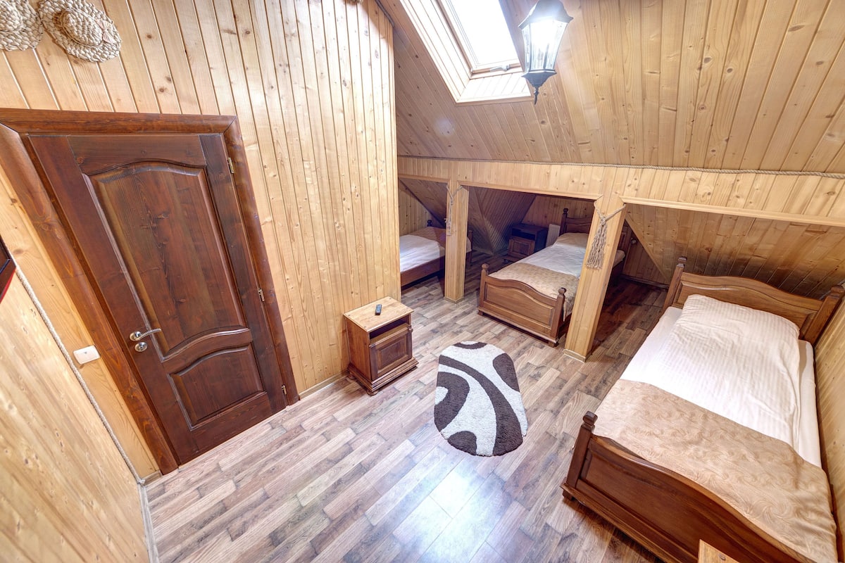 A wooden room with a sloped ceiling, a skylight, and three beds.