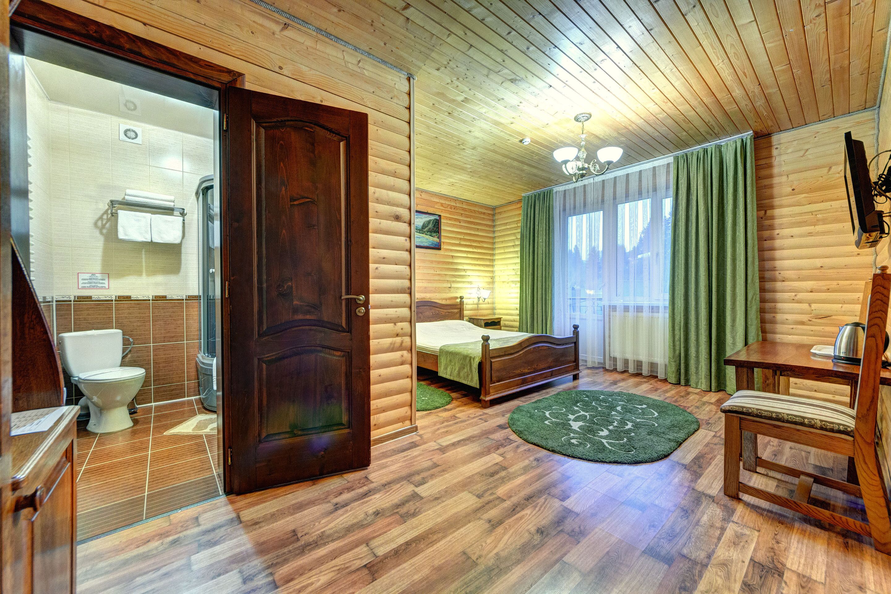 A log cabin-style room with a wooden door, a bed, a chair, a small table, and a view of the bathroom.