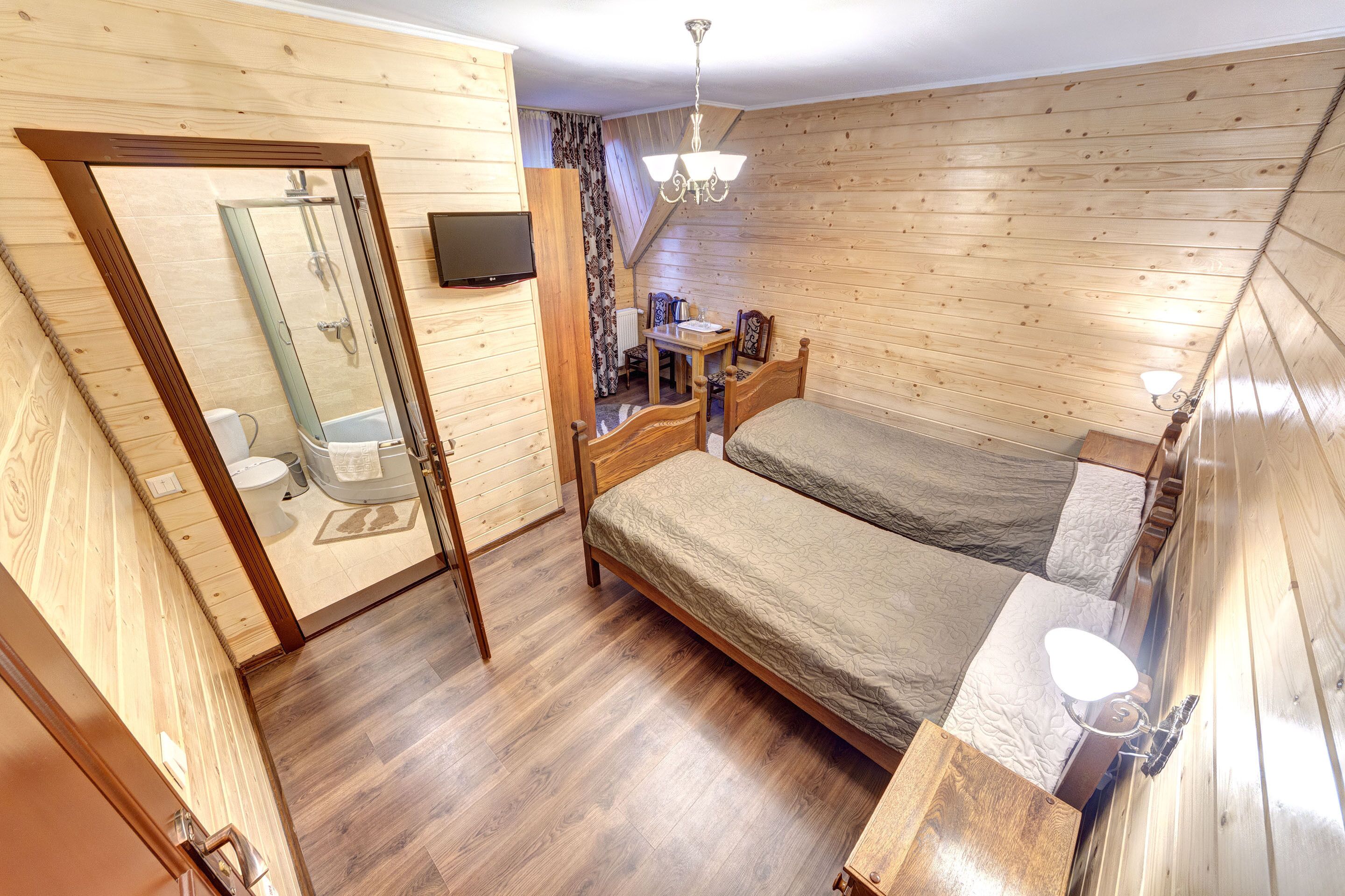 A wooden-paneled room with a bed, a bedside table, a mirror, and a shower area.