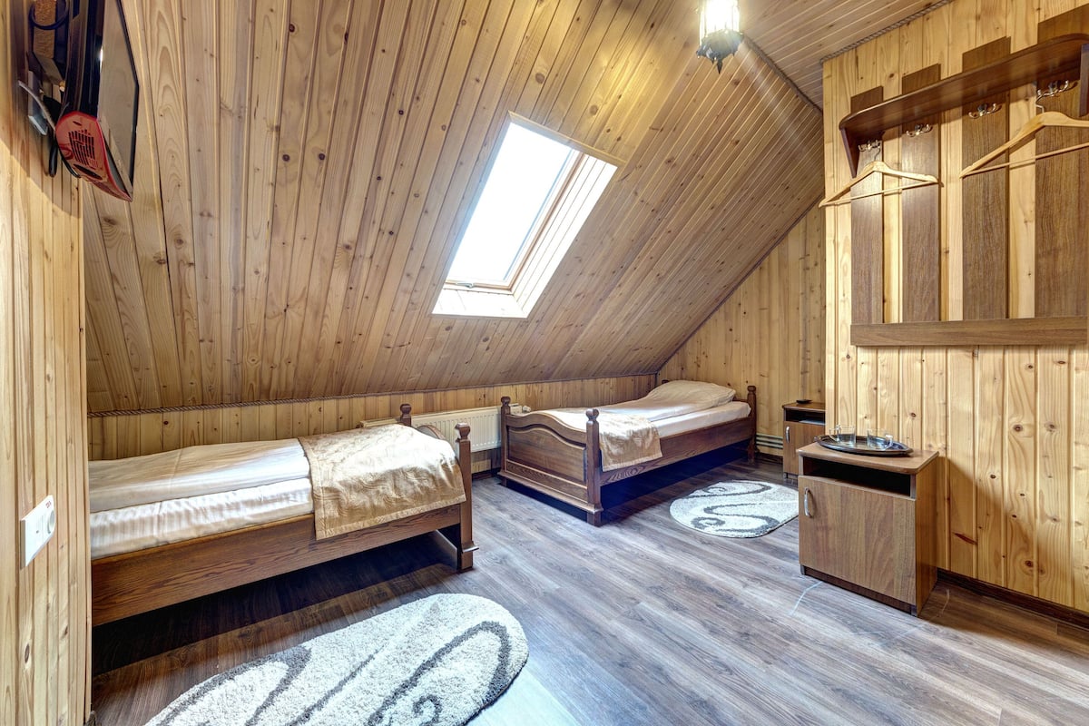 A wooden room with two beds, a small cabinet, and a skylight.