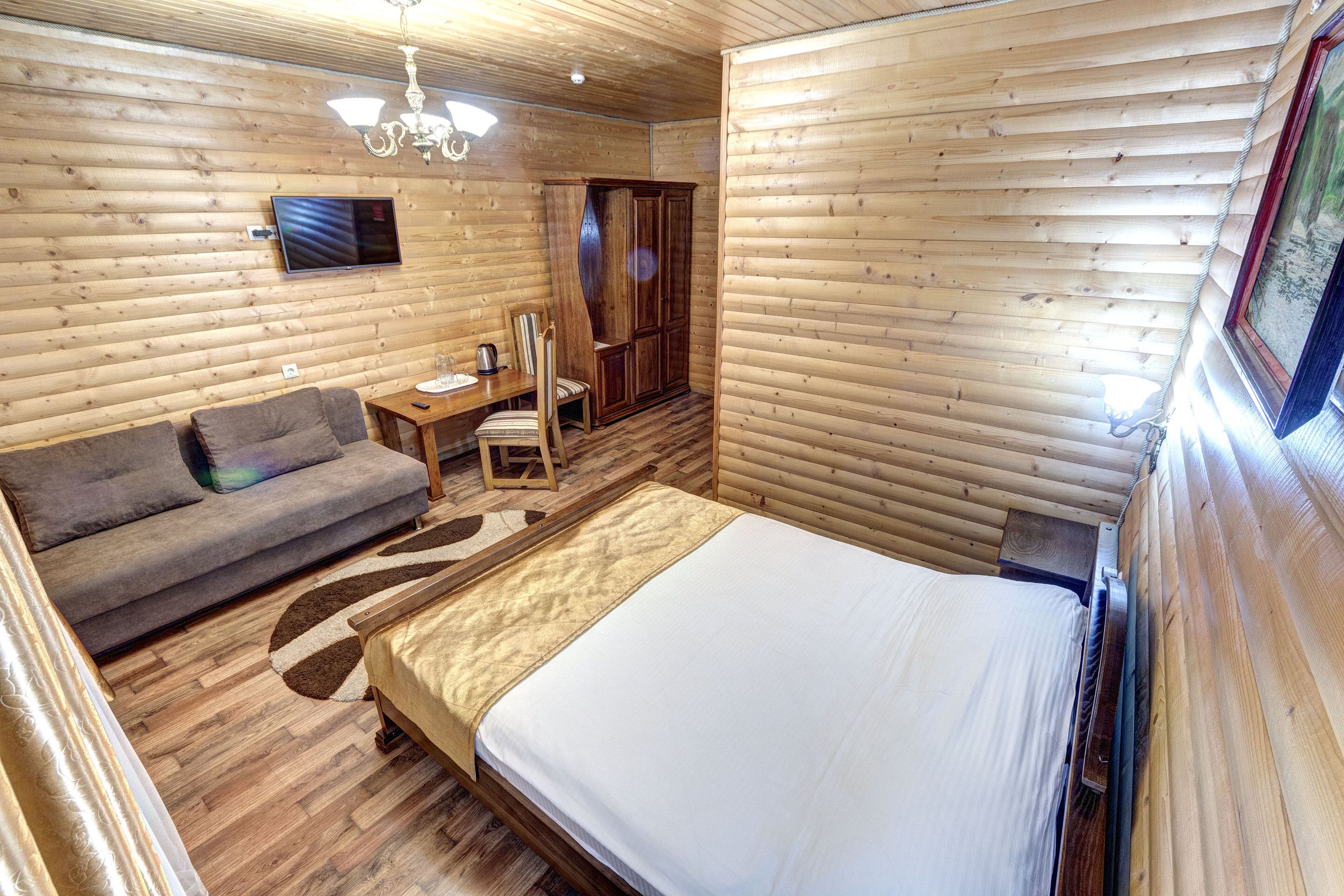 A wooden cabin room with a bed, a sofa, a desk, and a television.