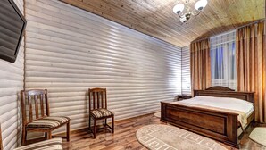 A bedroom with a wooden floor, a bed, a chair, a TV mounted on the wall, and a window with curtains. - Hotel Milli & Jon (Bukovel)