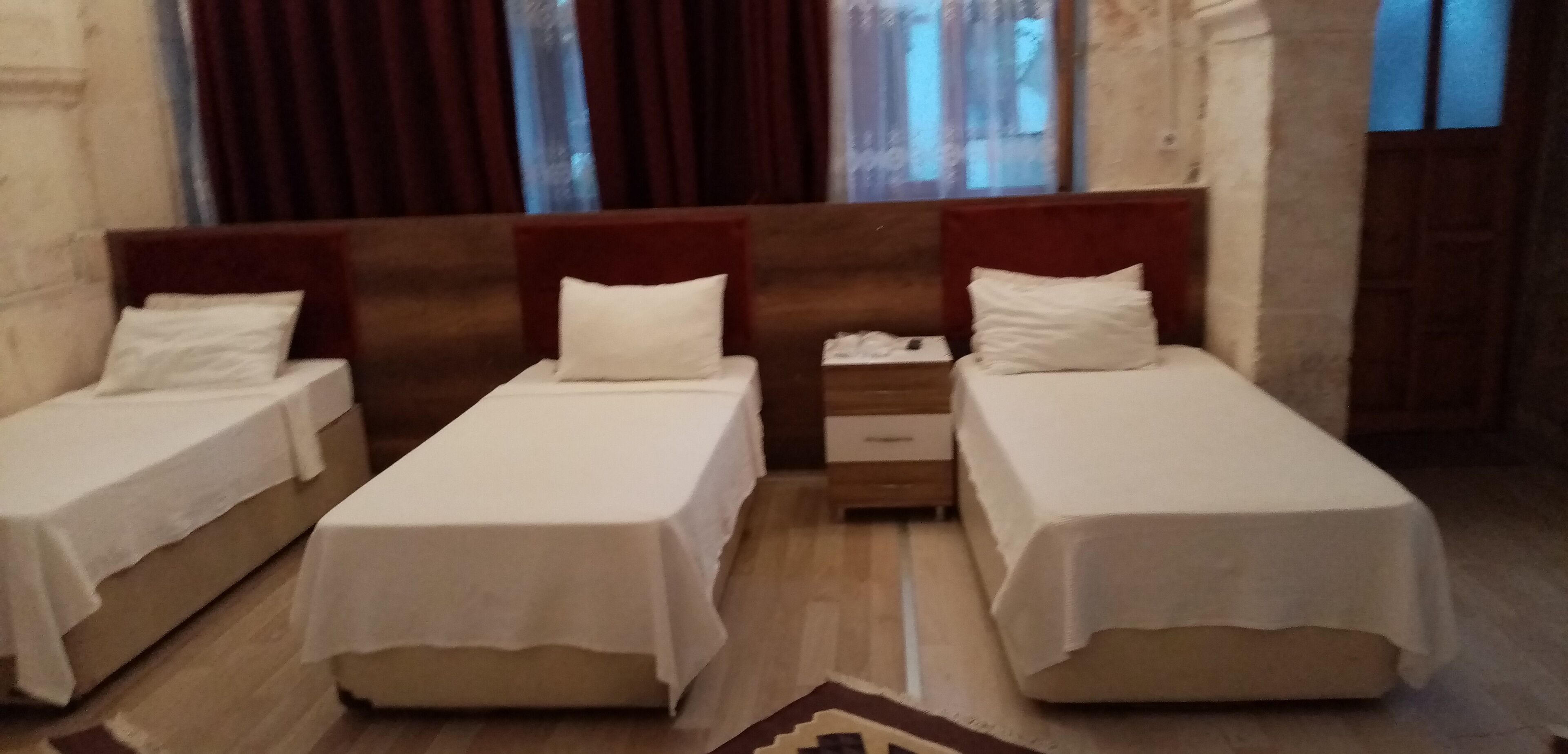 A hotel room with three single beds, wooden headboards, and a nightstand between the beds.