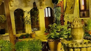Un pati amb una font, plantes en testos i un edifici amb arcs i un balcó.