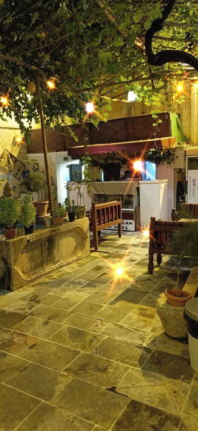 Une cour dallée de pierres, agrémentée de plantes en pot, d’un banc en bois et d’une enseigne indiquant « BAN HOTEL ».
