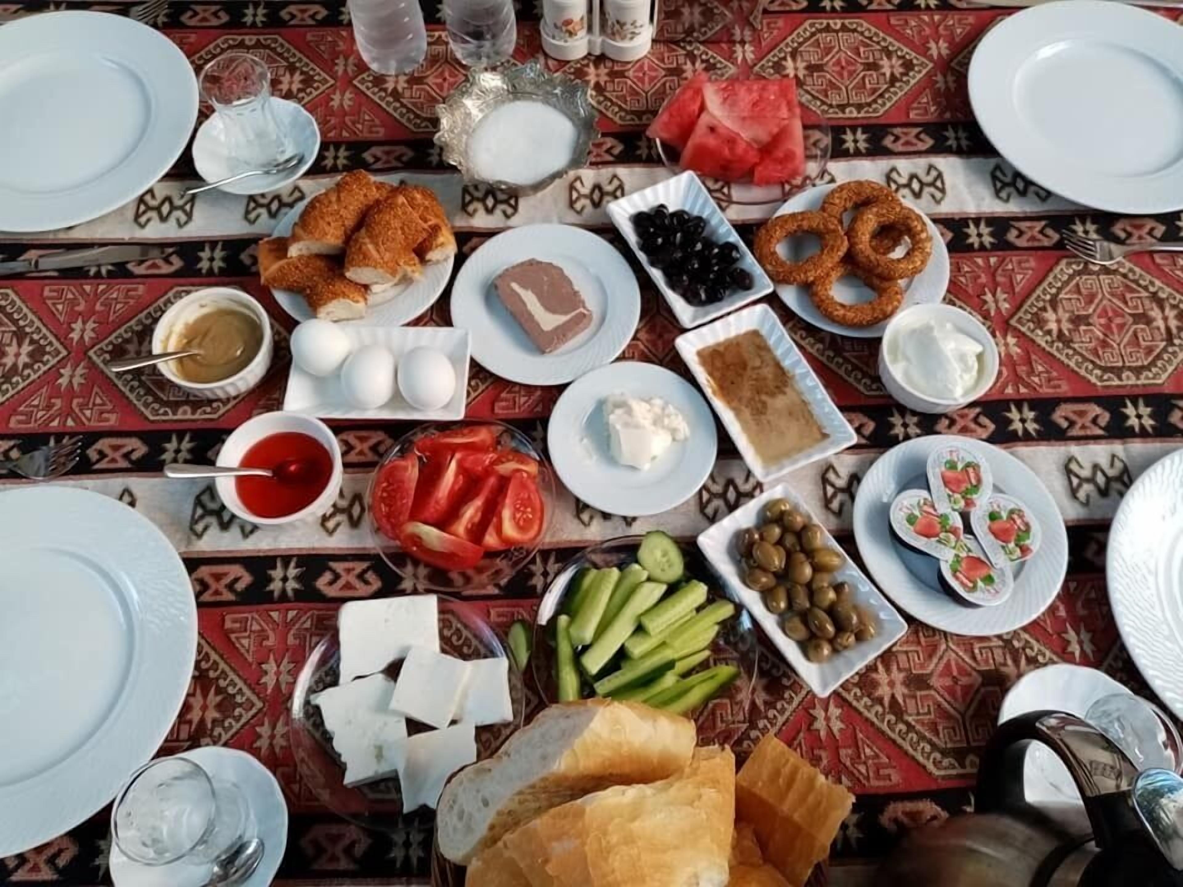 Une table dressée avec divers aliments, notamment du pain, des olives, des tomates, des concombres et du fromage.