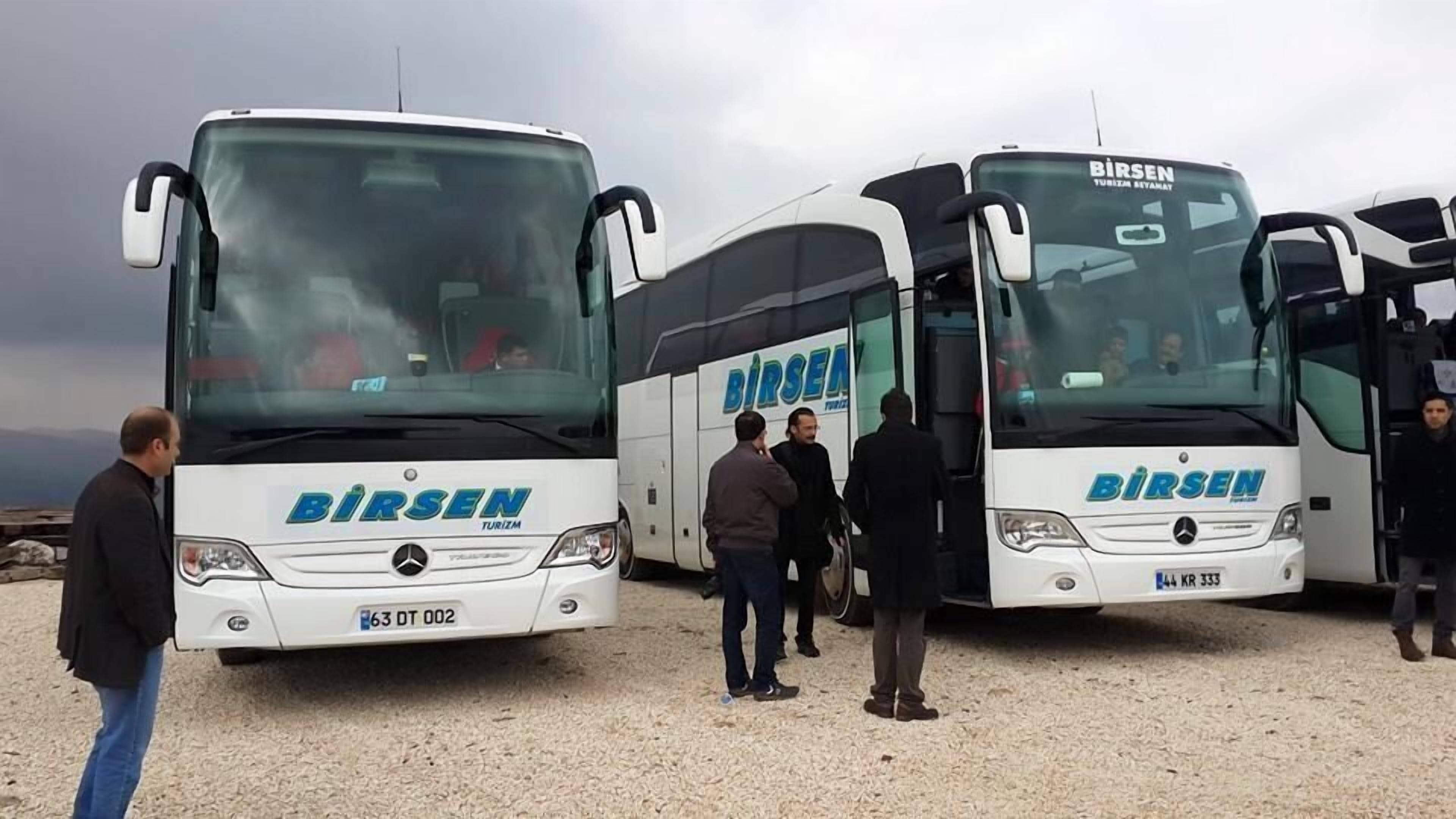 Three white buses with "BIRSEK TURIZM" branding parked on a gravel surface.